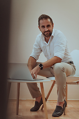 Image showing A confident businessman sitting and using laptop with a determined expression, while a beige background enhances the professional atmosphere, showcasing his productivity and expertise.