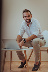 Image showing A confident businessman sitting and using laptop with a determined expression, while a beige background enhances the professional atmosphere, showcasing his productivity and expertise.