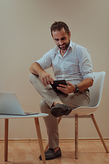 Image showing A confident businessman sitting and using tablet with a determined expression, while a beige background enhances the professional atmosphere, showcasing his productivity and expertise.