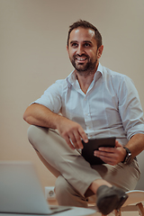 Image showing A confident businessman sitting and using tablet with a determined expression, while a beige background enhances the professional atmosphere, showcasing his productivity and expertise.