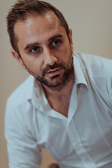 Image showing A confident businessman sitting while a beige background enhances the professional atmosphere, showcasing his productivity and expertise.