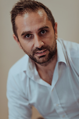 Image showing A confident businessman sitting while a beige background enhances the professional atmosphere, showcasing his productivity and expertise.