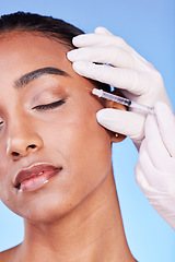 Image showing Needle, woman and face on blue background for beauty, skincare process and aesthetic filler in studio. Indian model, hands of surgeon and injection for plastic surgery, facial change or prp cosmetics