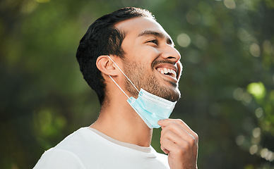 Image showing Smile, mask and remove with a man breathing fresh air in nature, feeling happy at the end of restrictions. Covid, freedom and post lockdown with a young person in the forest, woods or wilderness