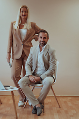 Image showing A business couple posing for a photograph together against a beige backdrop, capturing their professional partnership and creating a timeless image of unity and success.