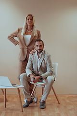 Image showing A business couple posing for a photograph together against a beige backdrop, capturing their professional partnership and creating a timeless image of unity and success.