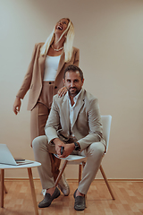 Image showing A business couple posing for a photograph together against a beige backdrop, capturing their professional partnership and creating a timeless image of unity and success.