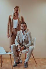 Image showing A business couple posing for a photograph together against a beige backdrop, capturing their professional partnership and creating a timeless image of unity and success.