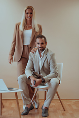 Image showing A business couple posing for a photograph together against a beige backdrop, capturing their professional partnership and creating a timeless image of unity and success.