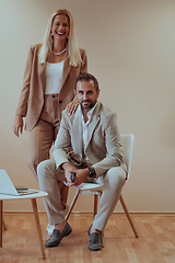 Image showing A business couple posing for a photograph together against a beige backdrop, capturing their professional partnership and creating a timeless image of unity and success.