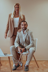 Image showing A business couple posing for a photograph together against a beige backdrop, capturing their professional partnership and creating a timeless image of unity and success.