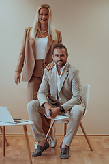 Image showing A business couple posing for a photograph together against a beige backdrop, capturing their professional partnership and creating a timeless image of unity and success.