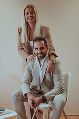 Image showing A business couple posing for a photograph together against a beige backdrop, capturing their professional partnership and creating a timeless image of unity and success.