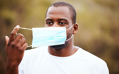 Image showing Corona, outdoor and black man remove mask, regulations and pandemic policy with breathing, health and decrease infection rates. African person, nature and guy take off face cover, safety and freedom