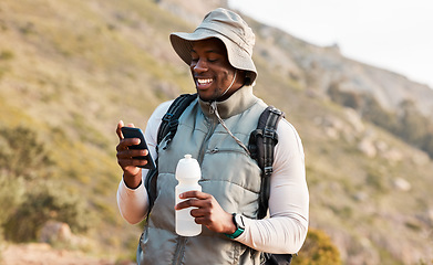 Image showing Hiking, water bottle and black man with a cellphone, smile or hydration with fitness, travel or health. African person, guy or hiker with a smartphone, mountain or thirsty with exercise or connection