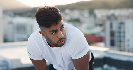 Image showing Fitness, city and tired man on a rooftop after running training, cardio workout and exercise outdoors. Runner, sports and healthy athlete exhausted with fatigue breathing or resting on a terrace