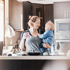 Image showing Happy mother and little infant baby boy together making pancakes for breakfast in domestic kitchen. Family, lifestyle, domestic life, food, healthy eating and people concept.