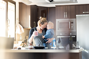 Image showing Happy mother and little infant baby boy together making pancakes for breakfast in domestic kitchen. Family, lifestyle, domestic life, food, healthy eating and people concept.