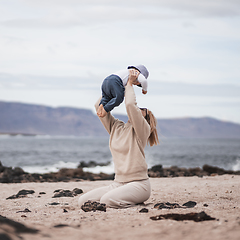 Image showing Mother enjoying winter vacations holding, playing and lifting his infant baby boy son high in the air on sandy beach on Lanzarote island, Spain. Family travel and vacations concept