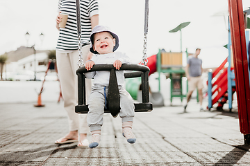 Image showing Mother pushing her infant baby boy child on a swing on playground outdoors.