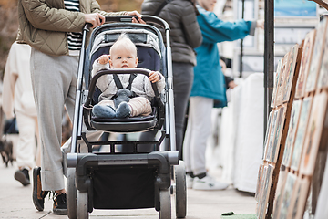 Image showing Mother walking and pushing his infant baby boy child in stroller in crowd of people wisiting sunday flea market in Malaga, Spain.