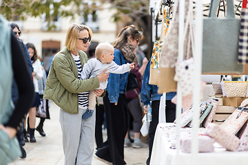 Image showing Mother walking carrying his infant baby boy child in crowd of people wisiting sunday flea market in Malaga, Spain