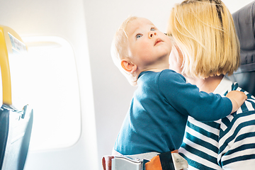 Image showing Mom and child flying by plane. Mother holding and playing with her infant baby boy child in her lap during economy comercial flight. Concept photo of air travel with baby. Real people.