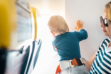 Image showing Mom and child flying by plane. Mother holding and playing with her infant baby boy child in her lap during economy comercial flight. Concept photo of air travel with baby. Real people.