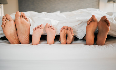 Image showing Feet, bed and family relaxing at their home for bonding, sleep and resting together on a weekend. Love, calm and closeup of parents laying with children in bedroom in the morning at modern house.
