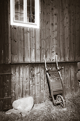 Image showing Old wooden wheelbarrow on a farm wall. Black and White photograp