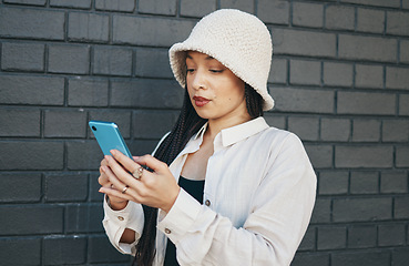 Image showing Girl with phone, brick wall and urban fashion, typing social media post, chat or internet search. Streetwear, gen z woman or online influencer with smartphone for content creation and communication.