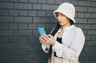 Image showing Woman with phone, wall background and streetwear, typing social media post, chat or internet search. Urban fashion, gen z girl or online influencer with smartphone for content creation and technology