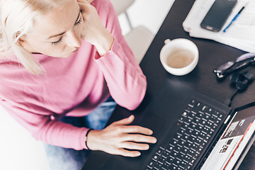 Image showing Female freelancer in her casual home clothing remotly working on laptop computer from her home while drinking her morning cup coffee. View from above