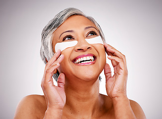 Image showing Senior, happy woman and face with eye patches in skincare, cosmetics or anti aging against a studio background. Mature female person or model smile with pads on eyes for facial treatment or routine