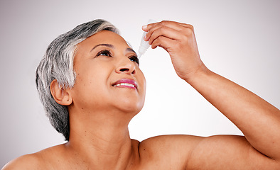 Image showing Senior woman, eye drops and body care with cosmetics, product or pharmaceutical against a studio background. Happy mature female person applying liquid to eyes for allergy, treatment or eyesight