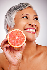 Image showing Senior, happy woman and face with grapefruit for vitamin C, skincare or natural nutrition against a studio background. Mature female person smile with organic citrus fruit for collagen, detox or diet