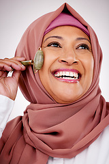 Image showing Muslim woman, facial roller and skin care in studio with quartz for dermatology, cosmetics and glow. Happy mature female person with islam hijab, face massage and beauty on a white background