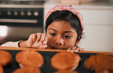 Image showing Baking, muffin and a sneaky indian girl in the kitchen of her home to steal a fresh pastry from the counter. Food, children or cooking with a young kid looking naughty at a baked snack closeup