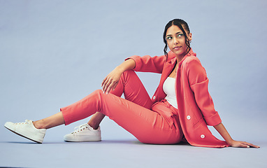 Image showing Woman, fashion and sitting on floor in studio with thinking face and makeup for beauty, aesthetic and cosmetics with mockup space. Smile, person and creative clothes on purple background with glow