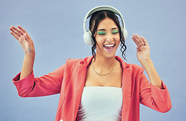 Image showing Dance, smile and woman with headphones, celebration and makeup on a blue studio background. Person, girl and model with headset, energy and streaming music with happiness, audio and song with sound