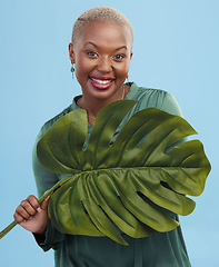 Image showing Black woman, monstera leaf and beauty, face with natural cosmetics and fashion on blue background. Silk green dress, eco friendly skincare and dermatology, African model glow and portrait in studio