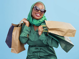 Image showing Shopping, sunglasses and black woman with bags, excited and boutique products on a blue studio background. African person, customer or model with luxury items, expensive clothes and rich with retail