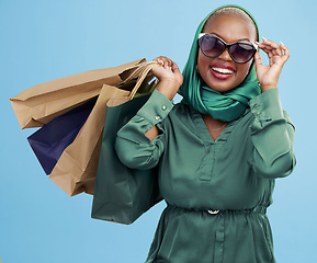 Image showing Studio bag, shopping and black woman excited for holiday fashion spree, commerce discount or boutique giveaway deal. Financial freedom, luxury product and wealthy African customer on blue background