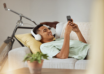 Image showing Headphones, phone video and man on a living room sofa happy and relax at home. Series, funny app and laughing with music and listening in a house lounge with web mobile streaming and couch with smile