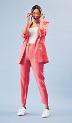 Image showing Fashion, portrait and young woman in studio with makeup, confidence and body in suit. Beauty, style and excited influencer girl in designer clothes, sunglasses and model standing on blue background.