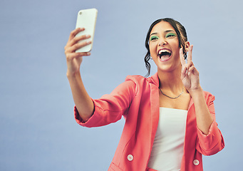 Image showing Smile, selfie and happy woman with a peace sign from social media and profile picture for creative job in studio. Influencer and makeup with career fashion with blue background and emoji hand gesture