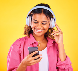 Image showing Headphones, phone and young woman in a studio listening to music, playlist or radio and networking. Happy, cellphone and female model from Mexico streaming a song or album by yellow background.