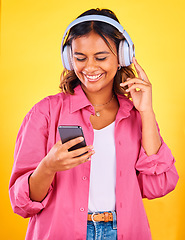 Image showing Headphones, cellphone and young woman in a studio listening to music, playlist or radio and networking. Happy, phone and female model from Mexico streaming a song or album by yellow background.