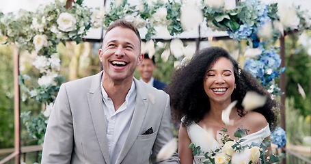 Image showing Couple, wedding and walk with flower confetti for event, celebration and outdoor in nature. Girl, happy interracial marriage and floral bouquet in park, holding hands or fist in air, pride or party