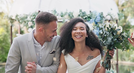 Image showing Couple, wedding and celebration with flower confetti for event, walk and outdoor in nature. Girl, happy interracial marriage and floral bouquet in park, holding hands or applause from crowd in aisle